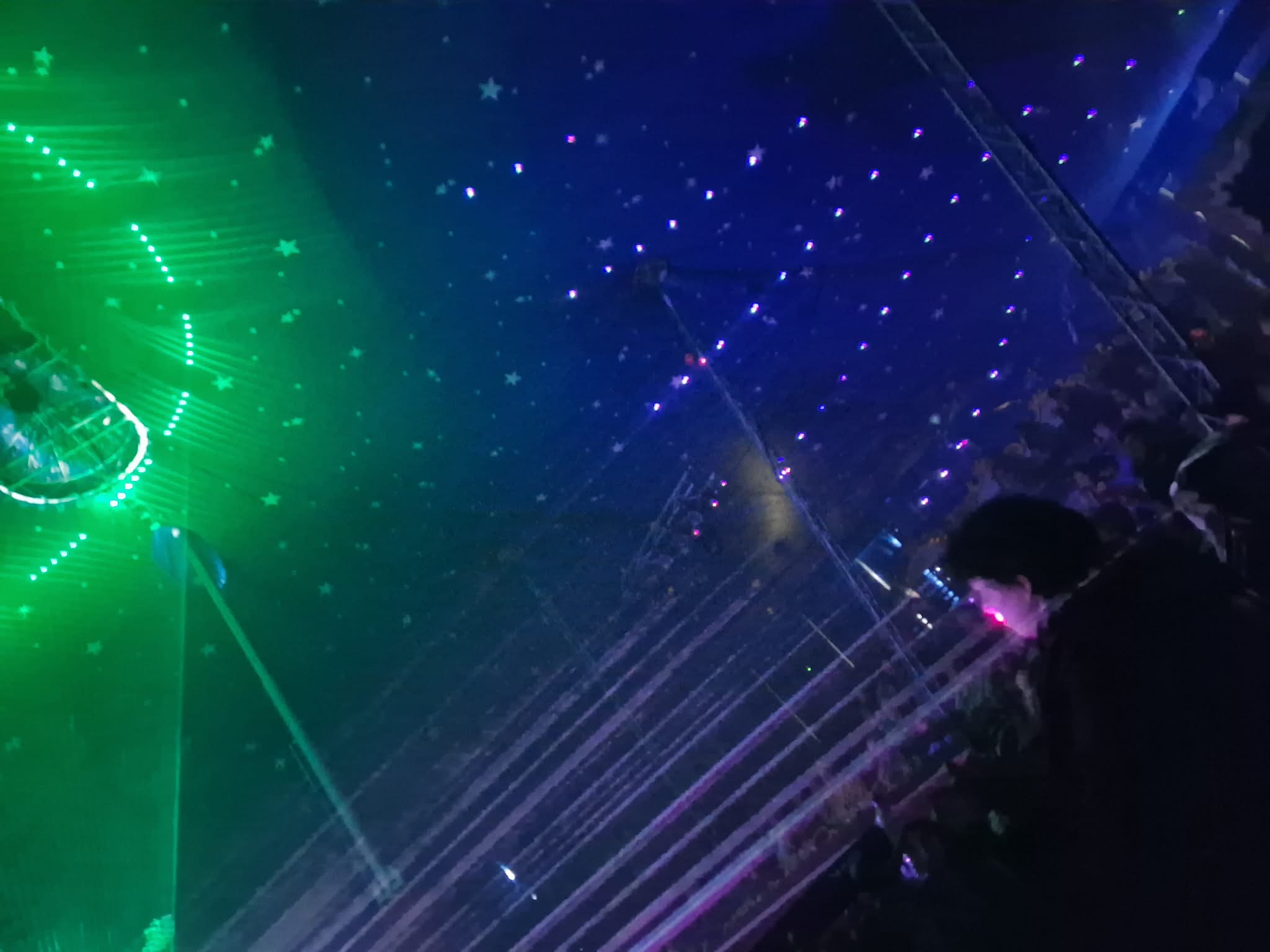 Sterrenprojectie en groene laser boven een mensenmassa — collectief ritueel onder een geconstrueerde hemel